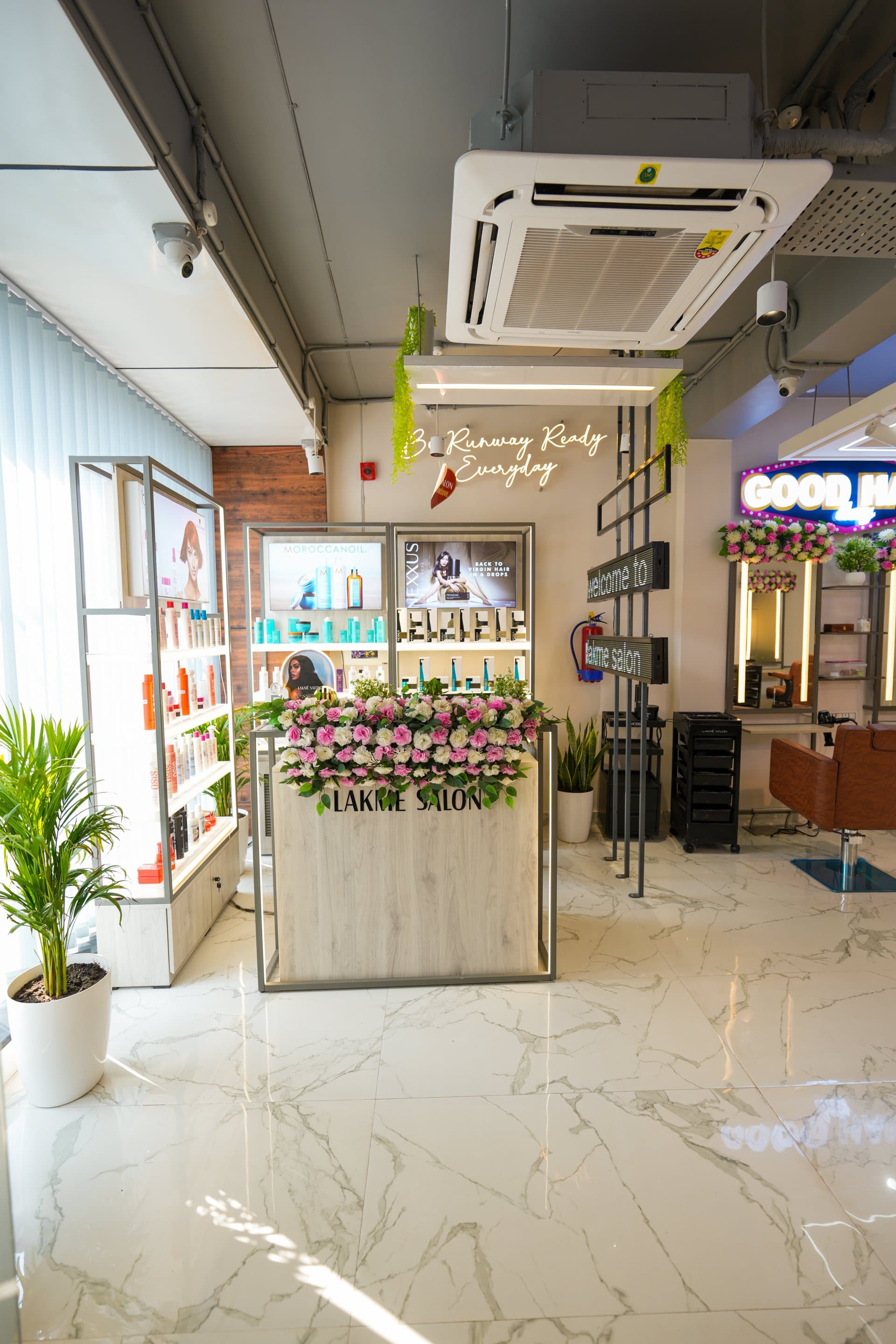 Reception at Lakmé Salon Rajajipuram, flower-topped desk and the professional retail wall